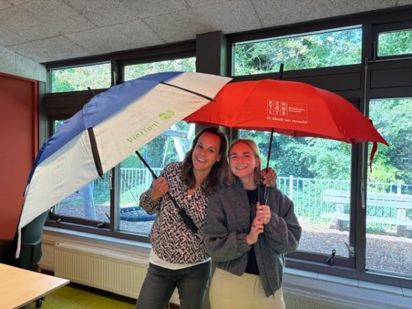 Maaike van Dalfsen en Eva Waij, ieder staand onder een paraplu, organiseren activiteiten over TOS ism Geen Kind de Buurt Uit